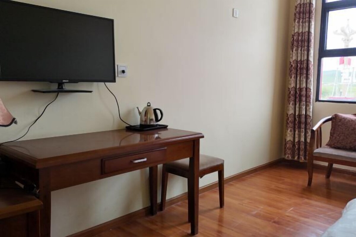 Een kamer met een houten bureau, een aan de muur bevestigde televisie, een stoel en een raam met gordijnen.