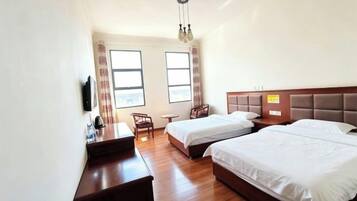 A hotel room with two beds, a desk, a chair, and a small table.