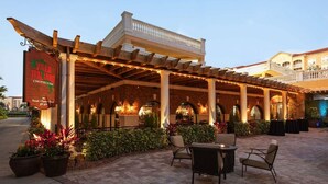 Ett utomhusområde med plats för att äta, en pergola, krukväxter och en skylt med texten ”Villa Italia Chophouse”.