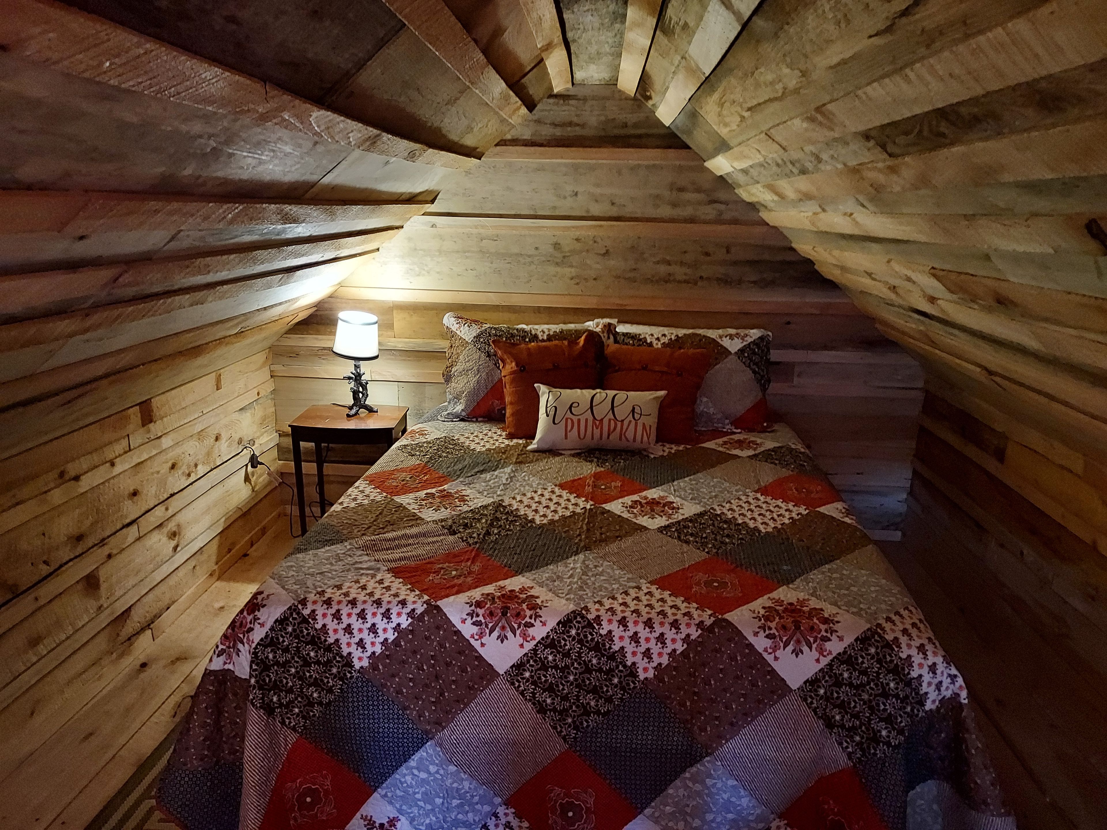 Una camera da letto mansardata accogliente con soffitto in legno, una coperta trapuntata e una lampada da comodino.