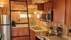 A wooden cabin interior with a kitchen area, including cabinets, a stove, and a sink.