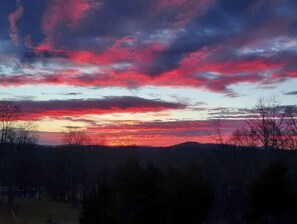Atardecer sobre un paisaje montañoso con pocos árboles y un cielo despejado.