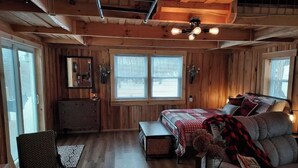 A cozy cabin-style bedroom with a bed, a chair, a dresser, and a window.