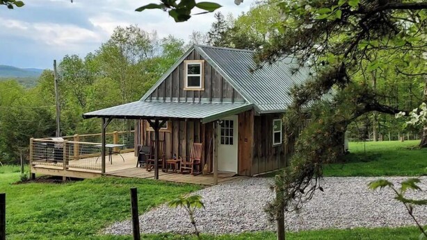 A rustic cabin with a metal roof, wooden walls, and a deck with outdoor furniture.