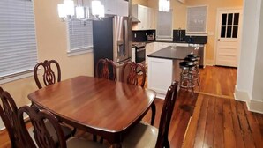 Uma sala de jantar com mesa e cadeiras de madeira, uma cozinha com armários brancos e um ventilador de teto.