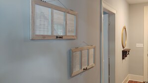 Um corredor com dois quadros informativos na parede, uma porta com espelho e um pequeno prateleira com objeto decorativo.
