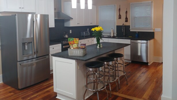 Cozinha moderna com eletrodomésticos de aço inoxidável, armários brancos, uma ilha central com banquetas e um lustre.