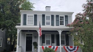 Uma casa de dois andares com varanda, uma bandeira americana e o número 18 na porta da frente.