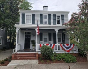 Ein zweistöckiges Haus mit Veranda, einer amerikanischen Flagge und der Hausnummer 18 an der Haustür.