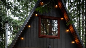 Une cabane dotée d’un bain à remous, d’un espace extérieur aménagé et d’une grande fenêtre donnant sur la forêt.