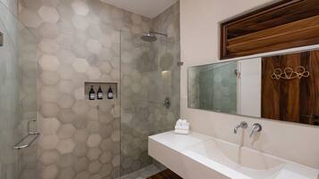 Un baño con pared de azulejos hexagonales, cabina de ducha de vidrio, tocador de madera con espejo y barra para toallas.