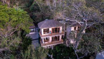 A two-story building with a thatched roof, surrounded by dense foliage.