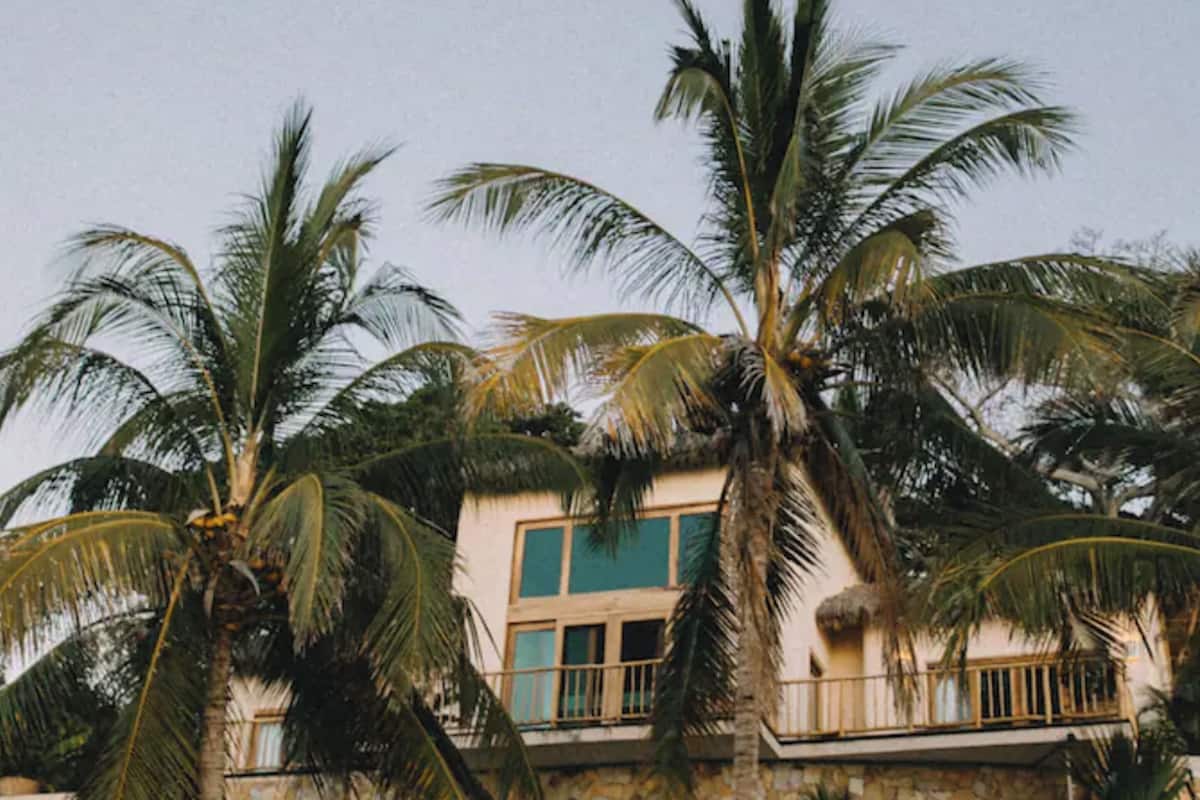 A building with a stone facade, a balcony, and palm trees in the foreground.
