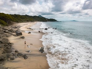 Una playa con costa rocosa, una persona caminando y una montaña al fondo.