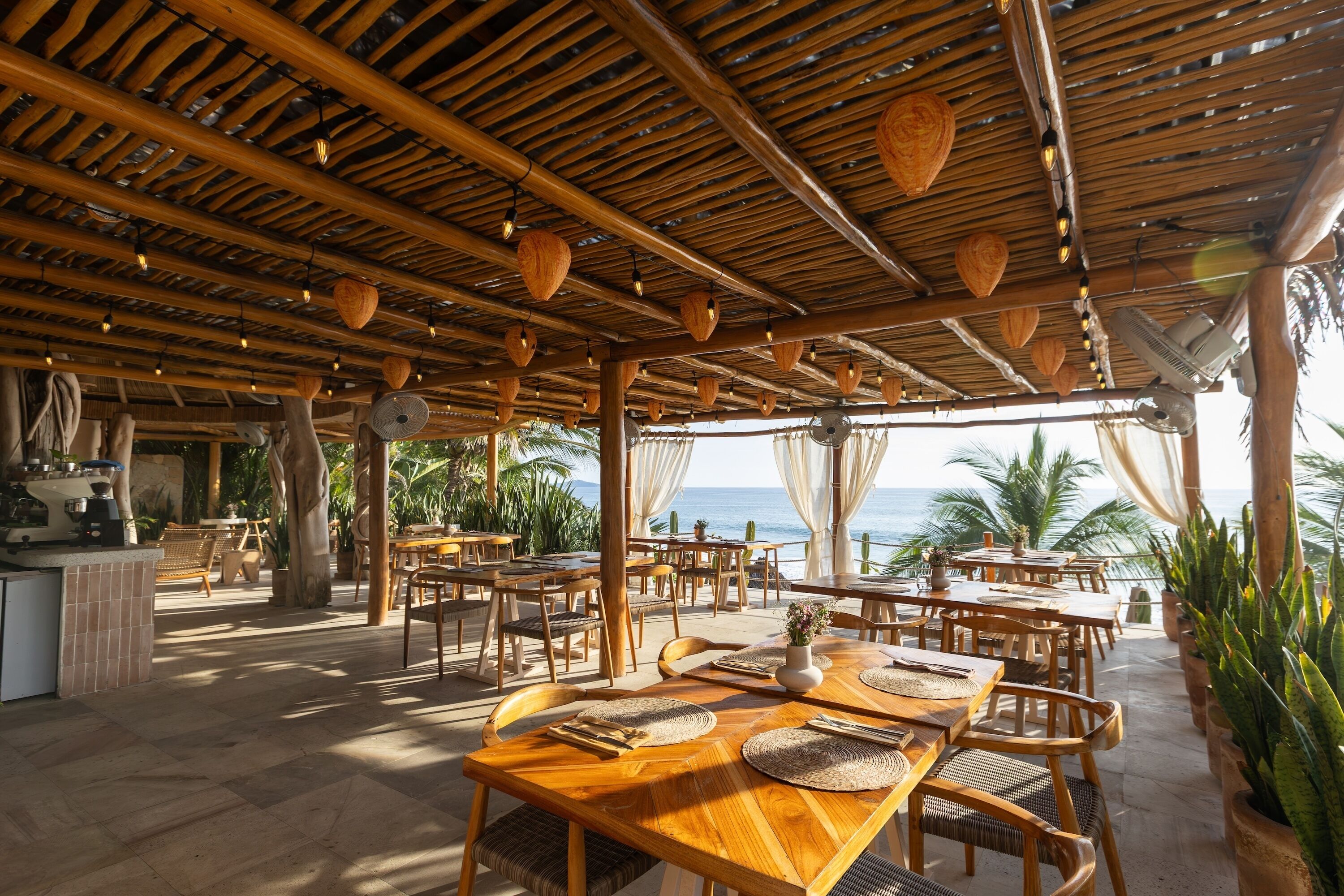 An outdoor dining area with wooden tables and chairs, a bar area, and a view of the ocean.