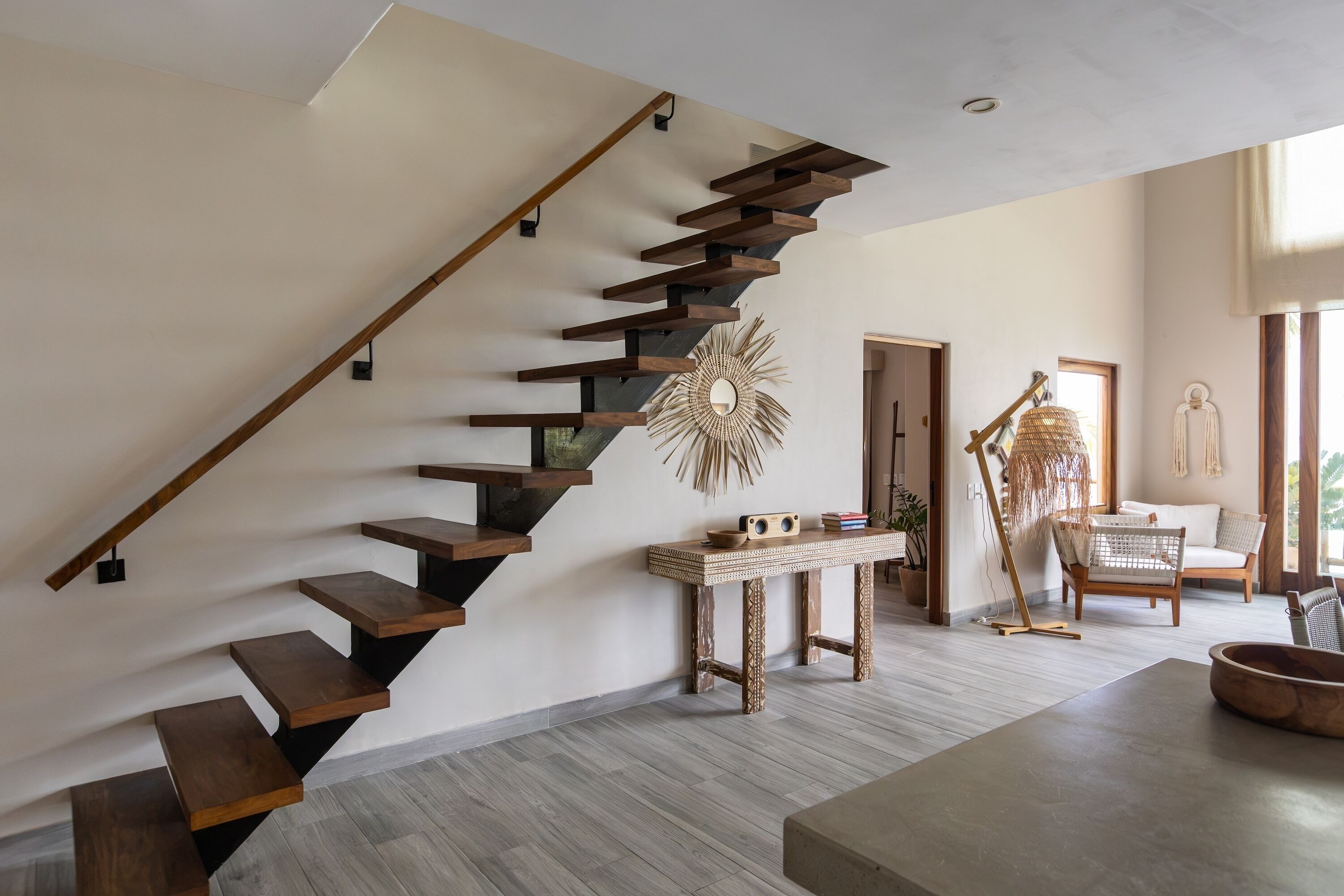 Un interior modern amb una escala de fusta, un mirall decoratiu i una zona de seients amb una cadira de fibra.