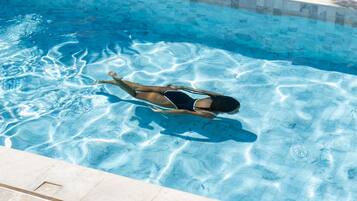 Una persona flotando en una piscina azul cristalina con borde de azulejos.