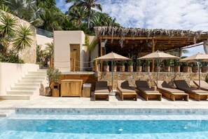 Zona de piscina con sillones de descanso, una pérgola de madera y plantas en macetas.