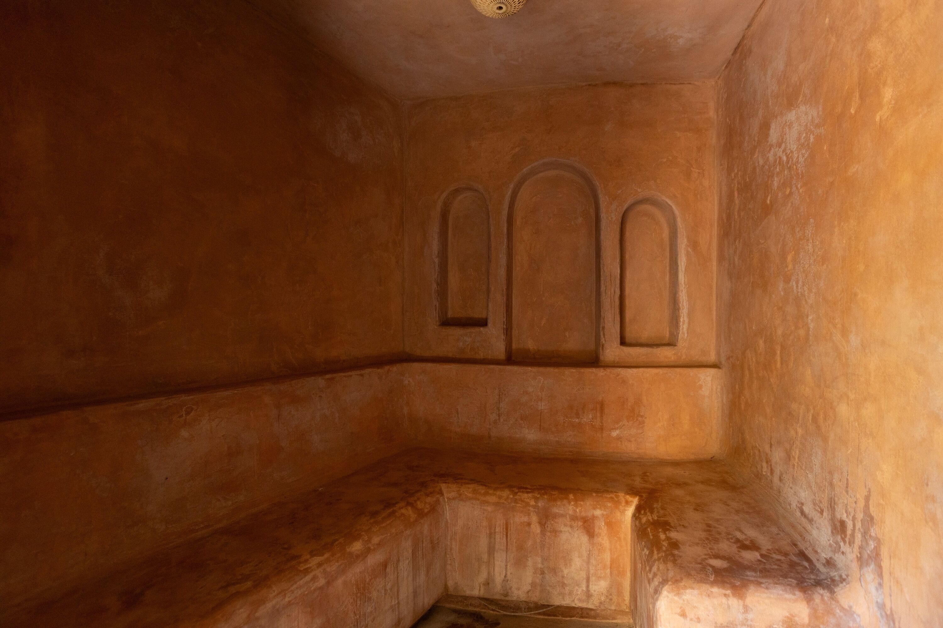 Quarto com teto baixo e um banco encostado na parede.
