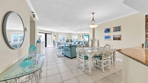 Uma sala de estar espaçosa com uma mesa de jantar de vidro, cadeiras brancas, sofá e luminária no teto.