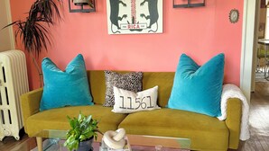 A living room with a mustard yellow sofa, teal cushions, a glass coffee table with books and a plant, a framed 'COSTA' artwork, and a radiator. - Private 2nd story apartment in the heart of Long Beach- Pura Vida! (Long Beach)