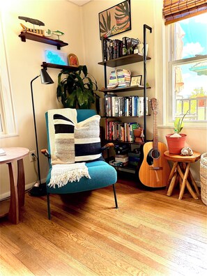 A cozy room with a blue armchair, a bookshelf, a guitar, and a window with a view. - Private 2nd story apartment in the heart of Long Beach- Pura Vida! (Long Beach)