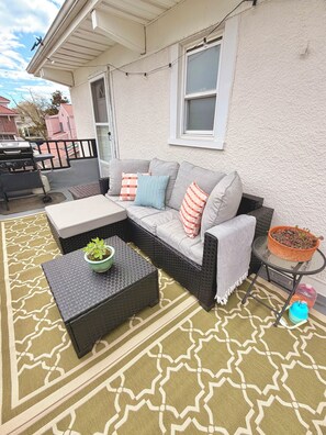 En terrasse med en grå modulsofa, et lille bord med en plante og en grill.
