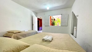 Une chambre avec deux lits, une fenêtre avec des volets et une porte donnant sur une autre pièce.