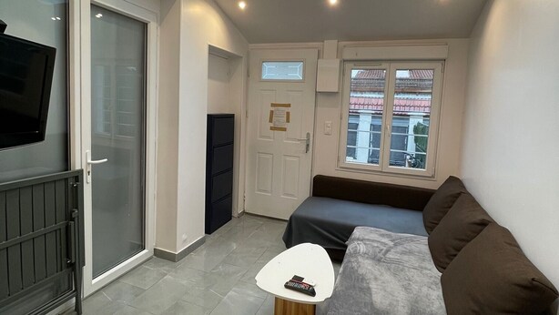 A compact living space with a skylight, a sofa, a small table, a TV, and a sliding glass door. - Maisonette Chaleureuse à la Porte de Paris 14 (Gentilly)