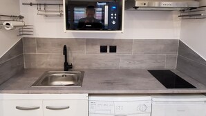 A compact kitchen with a built-in microwave, a sink, and a front-loading washing machine. - Maisonette Chaleureuse à la Porte de Paris 14 (Gentilly)