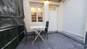 A small outdoor seating area with a table and two chairs, a white door, and a covered window. - Maisonette Chaleureuse à la Porte de Paris 14 (Gentilly)