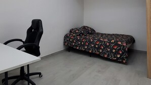 A room with a white ceiling, a black office chair, a sofa with a floral cover, and a wooden door. - Maisonette Chaleureuse à la Porte de Paris 14 (Gentilly)