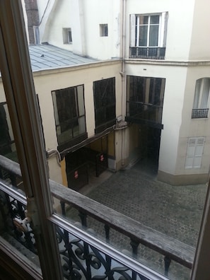 Une cour avec un sol carrelé, une balustrade en bois et un bâtiment doté de nombreuses fenêtres et d’une porte.