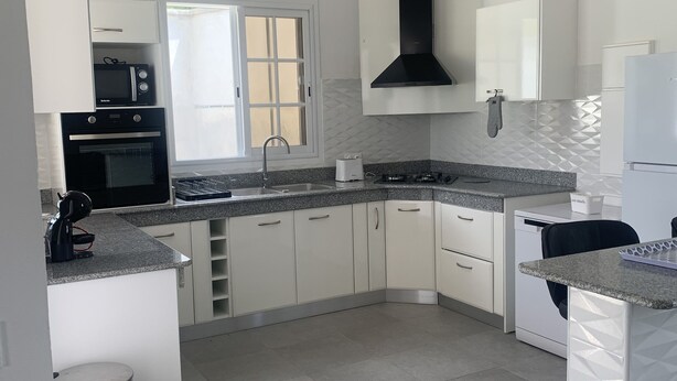 Una cocina moderna con armarios blancos, un lavamanos de acero inoxidable, horno empotrado y microondas.