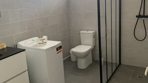 Un baño con inodoro, lavadora y cabina de ducha.
