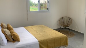 Un dormitorio con una cama, ventana, unidad de aire acondicionado y una silla.