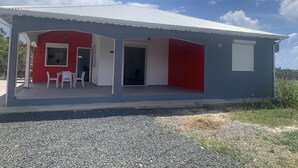Un edificio de dos pisos con fachada roja y gris, un porche cubierto con sillas blancas y un camino de entrada de grava.