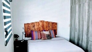 A bedroom with a wooden headboard, a bed with a white bedspread, a nightstand with a lamp, and a ceiling fan.