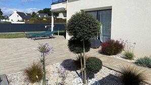 Een modern huis met balkon, een kleine boom en een tuin vol planten.