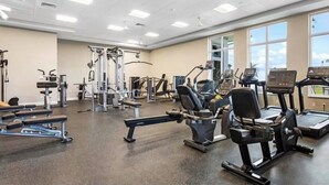 A gym with various exercise equipment, large windows, and a ceiling with recessed lighting.