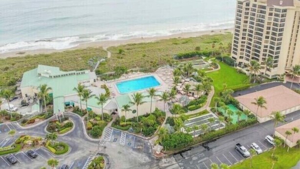 A resort with a swimming pool, a parking area, and a view of the beach and ocean.