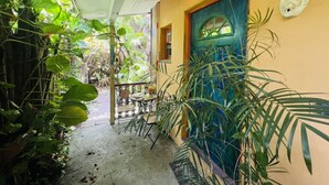 Un espacio al aire libre cubierto con una mesa y sillas, rodeado de abundante vegetación y una puerta azul.