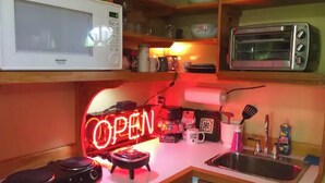 Una cocina con un letrero de neón que dice 'OPEN', un microondas, un tostador y varios utensilios de cocina sobre la encimera.