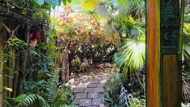 Un sendero en el jardín con losas de piedra, rodeado de frondosa vegetación y una cerca de madera.