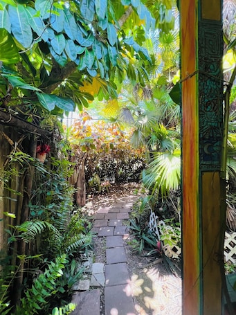 A garden pathway with stone tiles, surrounded by lush green foliage and a wooden fence.