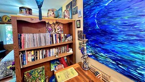 Una habitación con una estantería llena de libros, un cuadro grande de una escena abstracta en azul y una lámpara decorativa.