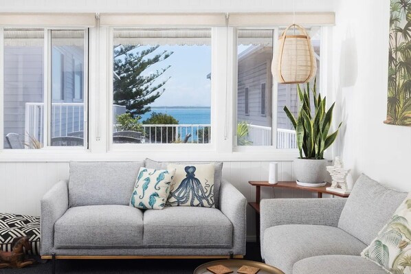 A living room with a grey sofa, a small side table, and a view of the ocean through large windows.