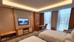Une chambre d’hôtel avec deux lits, une télévision, un bureau, une chaise et une fenêtre avec des rideaux.