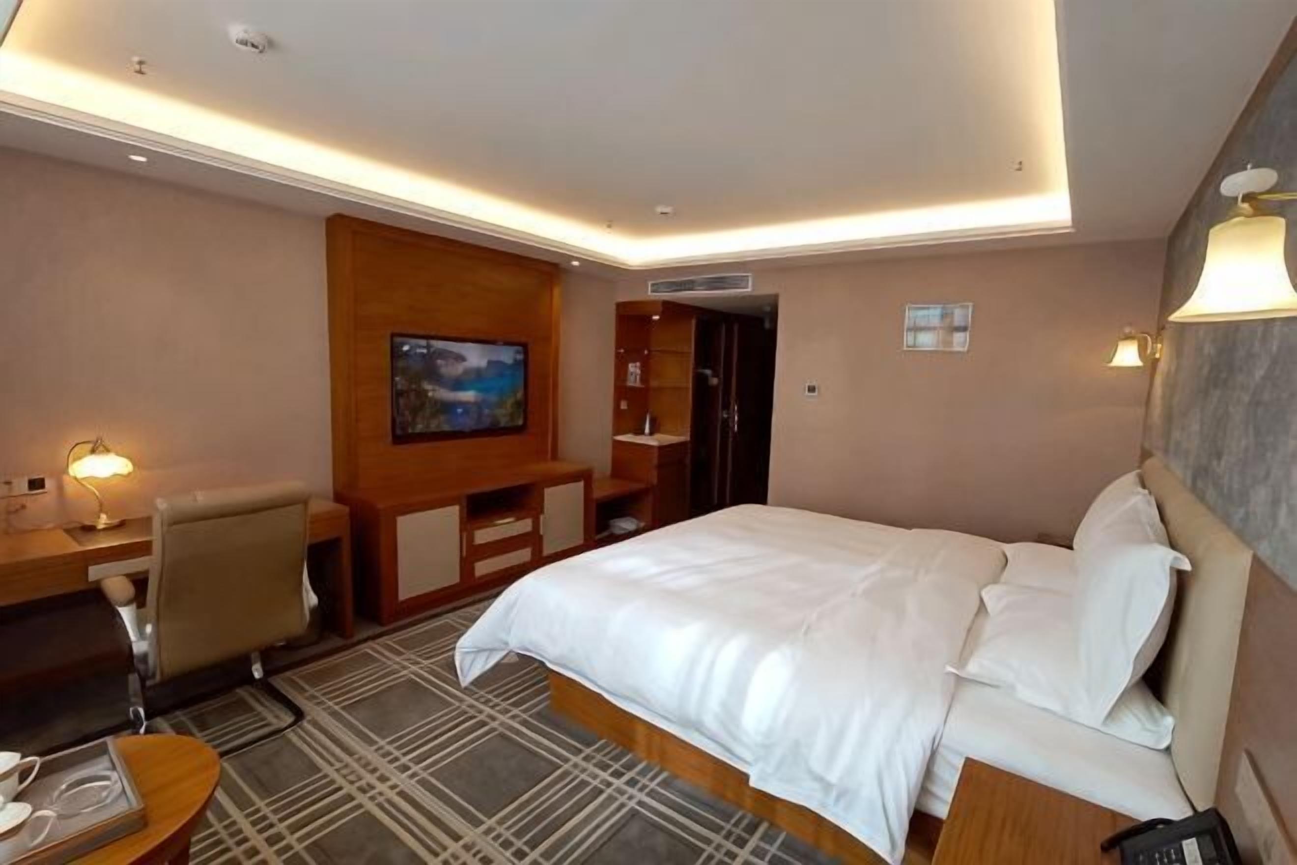 A hotel room with a bed, desk, chair, TV, and a view of the cityscape.