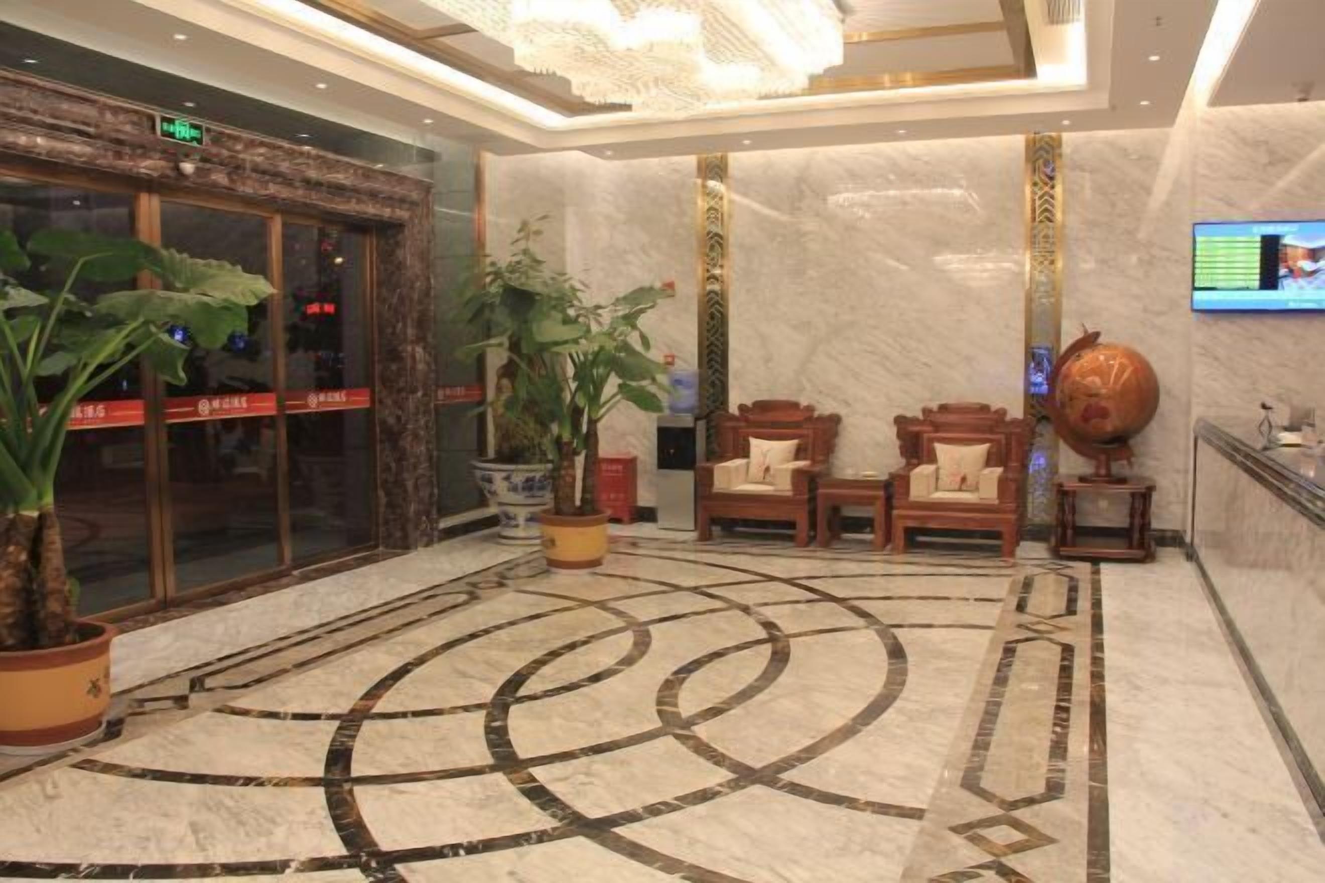 A lobby with a marble floor, two wooden chairs, a large potted plant, and a television on the wall.